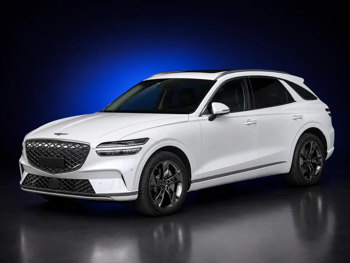 White Genesis Electrified GV70 JK1 electric SUV on a deep navy and cobalt studio background.